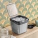 An OXO Good Grips plastic ice bucket with tongs and garnish tray filled with ice on a table.