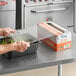 A person using Choice Foodservice Film to wrap a container of lettuce on a counter.