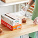 A person in a white apron using Choice Foodservice Film to wrap a box of food.