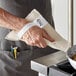 A man wearing a white apron using a WebstaurantStore terry cloth baker's pad to hold a hot pan.