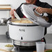 A man using an Avantco stainless steel lid to cook rice in a large metal container.