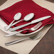 A Walco stainless steel dinner knife on a red napkin on a table with silverware.