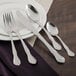 A close-up of a Walco Illustra stainless steel knife, spoon, and fork on a white plate.