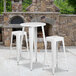 A white table with white metal legs and a round top with three white square seat backless stools underneath.