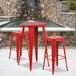 A red metal bar height table with 2 square seat backless stools.