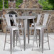 A Flash Furniture silver metal bar height table with four silver metal stools on an outdoor patio.