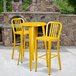 A yellow table with a black band and two yellow stools in front of a stone fireplace.