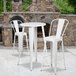 A Flash Furniture white metal table with two white bar stools in front of a stone fireplace.