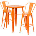 An orange metal bar height table with two orange metal bar stools.