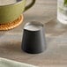 An American Metalcraft black satin stainless steel creamer with white liquid on a table.