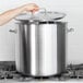 A hand using a Vollrath stainless steel lid to cover a large pot.