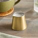 An American Metalcraft gold satin stainless steel creamer on a table with white liquid in it.