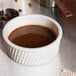 A Tuxton eggshell swirl ramekin filled with chocolate sauce on a counter.