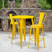 A yellow table with two yellow chairs and a yellow and grey stone wall.