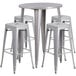 A silver metal bar height table with a white top and four square stools.