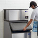 A man in a white shirt opening a container to put a water bottle into a Manitowoc air cooled ice machine.