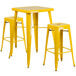 A yellow metal table with two yellow square seat bar stools.