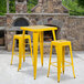 A yellow metal bar height table with 2 yellow metal square seat backless stools.