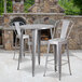 A Flash Furniture metal bar height table and two chairs on an outdoor patio with a fireplace.