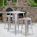 A Flash Furniture silver metal bar height table with two stools on an outdoor patio next to a stone fireplace.