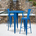 A blue metal bar height table with two blue metal bar stools with a hole in the back on an outdoor patio.