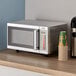 A Galaxy MW1000PB microwave on a counter next to coffee cups.