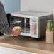A person holding a plate of food standing next to a Galaxy MW1000PB microwave.