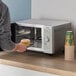 A man holding a plate of food in front of a Galaxy MW1000PD microwave.