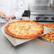 A chef using an American Metalcraft aluminum pizza peel to hold a pizza.