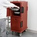 A man using a Cambro brick red Ultra Camcart to hold food pans in an outdoor catering setup.