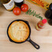 A pre-seasoned American Metalcraft mini cast iron skillet with cornbread in it next to a bottle of hot sauce.