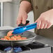 A person cooking food in a pan with blue Mercer Culinary tongs.