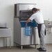 A man filling a large water container with ice from a Manitowoc air cooled ice machine.