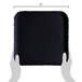 A hand holding a black square GET Mediterranean polycarbonate plate with a scalloped edge.