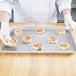 A person in white gloves holding a tray of cinnamon rolls.