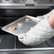 A person in gloves holding a Chicago Metallic aluminum sheet pan of cinnamon rolls on a counter in a professional kitchen.