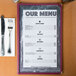 A black menu with an angled marble border on a table in an Italian restaurant.
