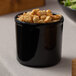 A black Cal-Mil melamine condiment jar filled with croutons on a table in a salad bar.