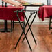 A man using a Tablecraft black metal tray stand to hold a tray of food on a table with a red tablecloth.