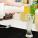 A person pouring liquid from a Carlisle white and yellow bottle into a glass.