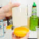 A person pouring liquid from a plastic bottle with a yellow lid into a white container.