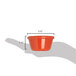 A hand holding a small orange Carlisle ramekin with measurements.