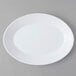 An Arcoroc white opal oval platter with a white rim on a gray surface.