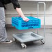 A person using a grey Cambro Camdolly with a blue dish rack.