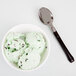 A bowl of mint chocolate chip ice cream with a WNA Comet Reflections Duet stainless steel look plastic spoon.