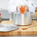 A person using a Vollrath aluminum sauce pan to pour orange carrots onto a table.