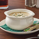 An Acopa ivory stoneware bowl of onion soup with green herbs on top sitting on a plate.