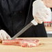 A person using a Dexter-Russell narrow fillet knife to cut a piece of meat on a wooden surface.