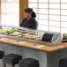 a person standing behind a counter with a display of sushi