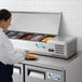 A woman in a white coat using an Avantco Countertop Refrigerated Prep Rail on a counter.